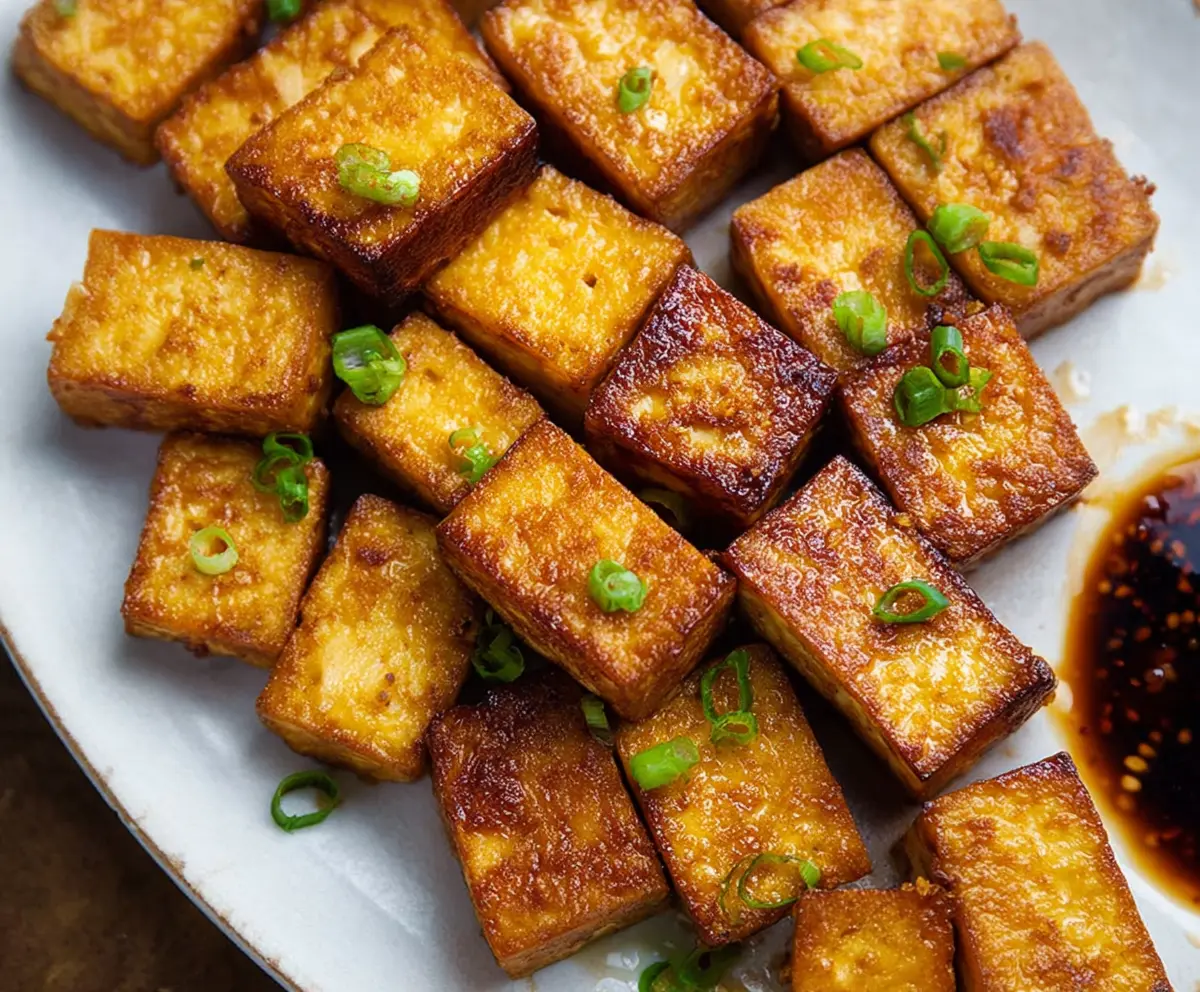 Golden crispy baked tofu served with fresh vegetables and dipping sauce for a healthy vegan meal.