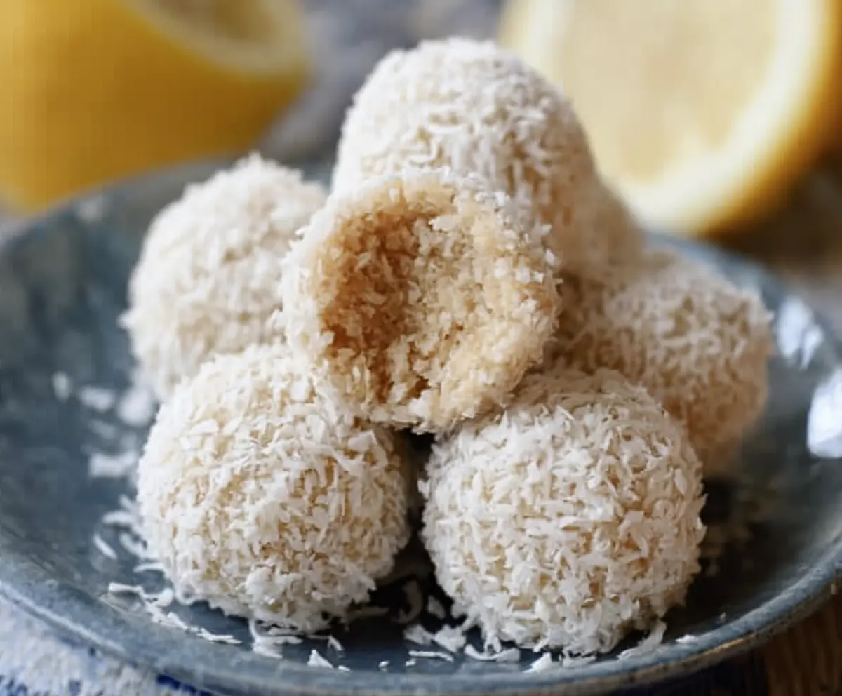 Close-up of lemon coconut protein balls on a plate, highlighting their textured surface and fresh coconut garnish.